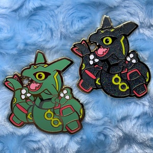 Può includere: Due spille smaltate con versioni cartoon del Pokémon Rayquaza. Una spilla è verde con accenti rossi e l'altra è nera con accenti rosa. Entrambe le spille hanno una finitura lucida e scintillante.