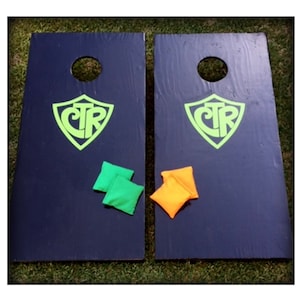 May include: Two black wooden cornhole boards with green and orange bean bags. The boards have a green shield with the letters "CTR" in white.