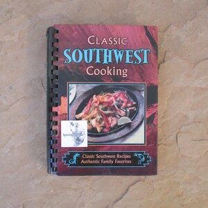 May include: A spiral-bound cookbook titled "Classic Southwest Cooking" with a maroon and blue cover. The cover features an image of a sizzling fajita dish. The book also includes the text "Classic Southwest Recipes Authentic Family Favorites".