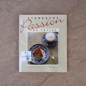 May include: A cookbook titled "Starbucks Passion for Coffee" with a cream-colored cover. The cover features a coffee cup, a slice of cake on a blue plate, and the text "A Starbucks Coffee Cookbook".