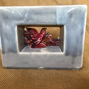 May include: A gray ceramic vase with a rectangular opening featuring a red bird figurine inside. The vase has a glazed finish and a modern design.
