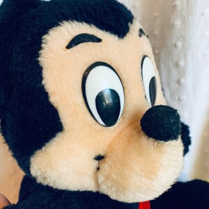 May include: A black and tan plush toy with large black eyes and a black nose. The toy is wearing a red and yellow shirt.