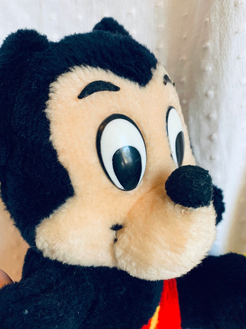 May include: A black and tan plush toy with large black eyes and a black nose. The toy is wearing a red and yellow shirt.