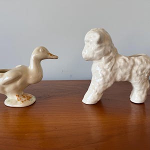 May include: Two ceramic planter figurines, one shaped like a duck and the other like a sheep. Both are white with a glazed finish.