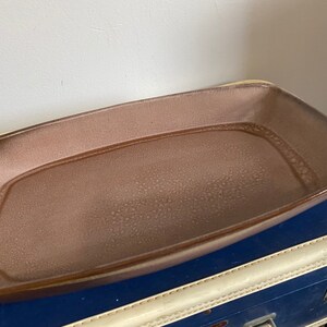 May include: A large, rectangular serving dish made of brown ceramic with a speckled glaze. The dish has a slightly raised rim and a smooth, glossy finish.