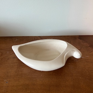 May include: White ceramic bowl with a unique, abstract shape. The bowl is smooth and has a slightly curved lip.