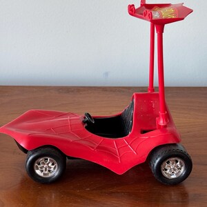 Pu&ograve; includere: Macchina giocattolo di plastica rossa con un design a ragnatela e un'antenna rossa alta con un cartello giallo che dice "Spider-Man".