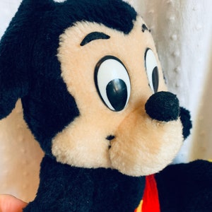 May include: A vintage plush Mickey Mouse toy with black fur, large black eyes, a brown nose, and red shorts with yellow buttons.