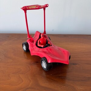 Pu&ograve; includere: Macchina giocattolo rossa con una figura di Spider-Man al volante. La macchina ha una cappotta rossa e ruote nere.