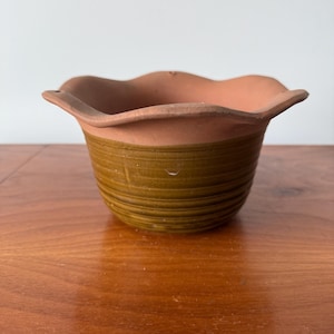 Könnte beinhalten: Ein kleiner Terrakotta-Blumentopf mit einem gewellten Rand und brauner und grüner Glasur.