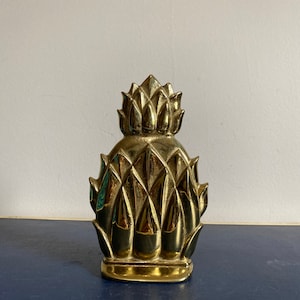 Peut inclure: Un arrêt de porte en forme d'ananas doré. L'arrêt de porte est en laiton massif et présente un design détaillé.