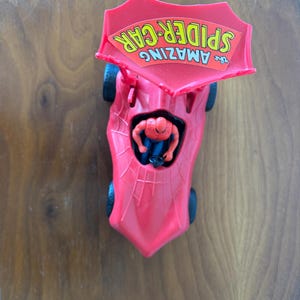Pu&ograve; includere: Macchina giocattolo di plastica rossa con un design a ragnatela e un cartello giallo e rosso con la scritta "The Amazing Spider-Car" sulla parte superiore. Una figura di Spider-Man rossa e blu &egrave; seduta sul sedile del conducente.