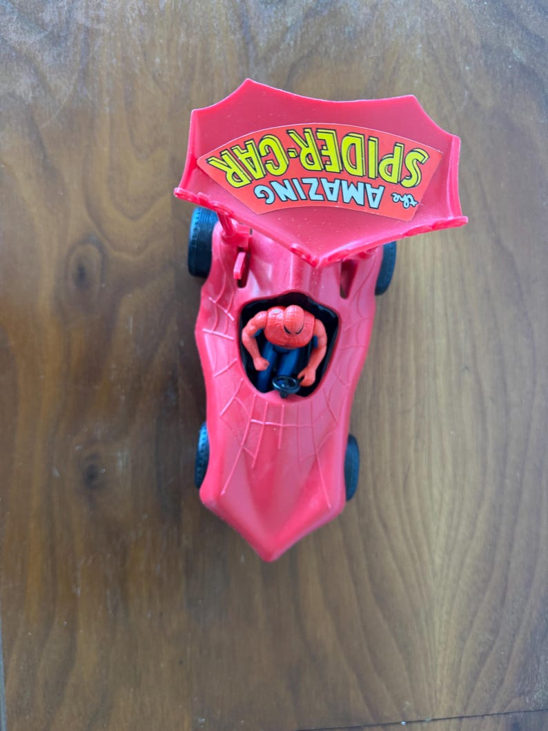 Pu&ograve; includere: Macchina giocattolo di plastica rossa con un design a ragnatela e un cartello giallo e rosso con la scritta "The Amazing Spider-Car" sulla parte superiore. Una figura di Spider-Man rossa e blu &egrave; seduta sul sedile del conducente.