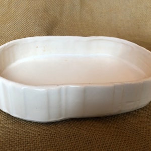 Puede incluir: Plato ovalado de cerámica blanca con un diseño acanalado. El plato está vacío y tiene una ligera curva en la parte inferior.