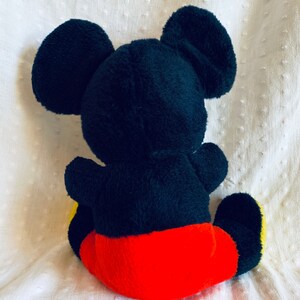 May include: A black plush Mickey Mouse toy with red shorts and yellow shoes. The toy is sitting on a white surface.