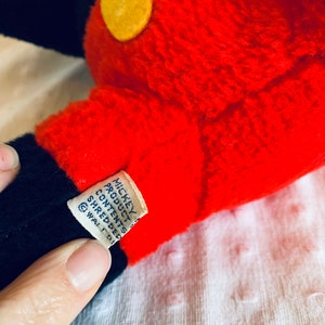 May include: Close-up of a red and black Mickey Mouse plush toy with yellow felt circles. The tag reads "Mickey Product Contents Shredded  &copy; Walt D.  ",