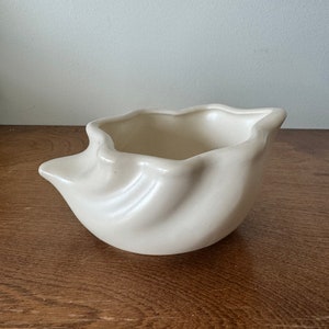 May include: A white ceramic planter shaped like a seashell. The planter has a smooth, glossy finish and a slightly wavy texture.