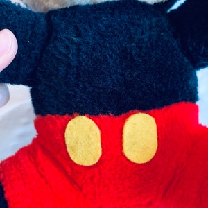 May include: A plush Mickey Mouse toy with black fur, red shorts, and yellow buttons. The toy has a white face and black eyes.