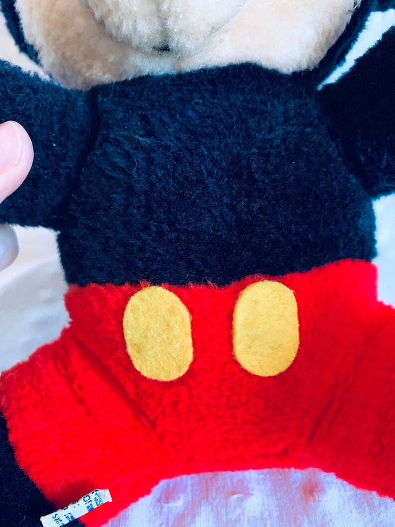 May include: A plush Mickey Mouse toy with black fur, red shorts, and yellow buttons. The toy has a white face and black eyes.