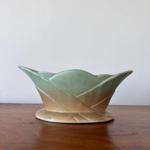 May include: A green and brown ceramic planter with a woven design. The planter has a wide, rounded base and a flared top.