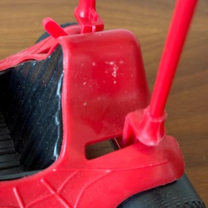 Pu&ograve; includere: Un'auto giocattolo di plastica rossa con ruote nere e un design a ragnatela. L'auto ha due pali rossi che si estendono dalla parte posteriore.