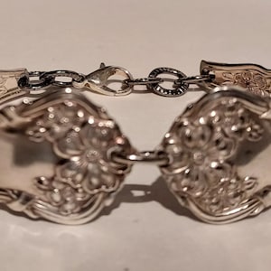 May include: A silver bracelet made from two vintage spoons, connected by a silver chain. The spoons have ornate floral designs.