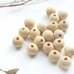 May include: A collection of 18 natural wood beads, each with a hole drilled through the centre. The beads are round and smooth, with a light brown colour.
