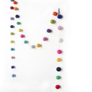 Puede incluir: Dos guirnaldas de bolas de fieltro de colores colgadas en una pared blanca. La guirnalda est&aacute; hecha de peque&ntilde;as bolas de fieltro redondas de varios colores, incluyendo rojo, naranja, amarillo, verde, azul, morado y rosa.