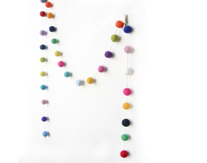 Puede incluir: Dos guirnaldas de bolas de fieltro de colores colgadas en una pared blanca. La guirnalda est&aacute; hecha de peque&ntilde;as bolas de fieltro redondas de varios colores, incluyendo rojo, naranja, amarillo, verde, azul, morado y rosa.