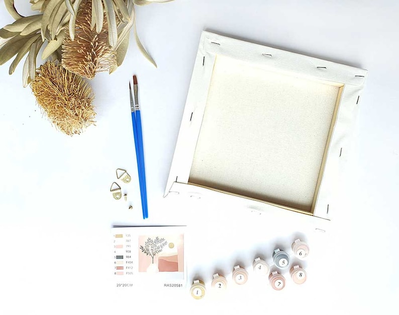 Puede incluir: Kit de pintura por n&uacute;meros con un lienzo, pinceles y botes de pintura numerados del 1 al 8. El lienzo es blanco y los botes de pintura son de varios tonos de rosa, beige y gris. El kit incluye un dise&ntilde;o de un &aacute;rbol con un sol y formas abstractas en tonos de rosa y beige.