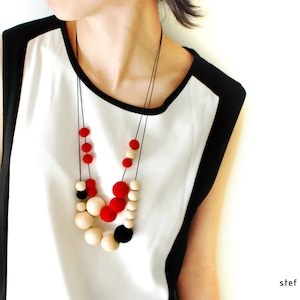 May include: A woman wearing a white and black shirt with a layered necklace of red, black, and cream colored beads.