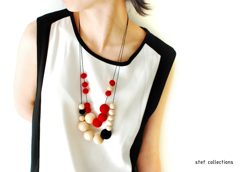 May include: A woman wearing a white and black shirt with a layered necklace of red, black, and cream colored beads.