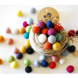 May include: A collection of colorful felt balls arranged in a nest of twine. The balls are in various colors, including red, orange, yellow, green, blue, purple, and white. A small tag with the text "Stef Collections Melbourne" is attached to the twine nest.
