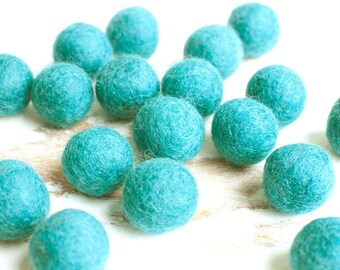 May include: A collection of teal felt balls, scattered on a white surface. The balls are soft and fluffy, and they are perfect for crafting or decorating.