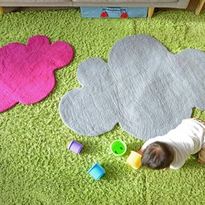 May include: Two fluffy cloud-shaped rugs in pink and grey on a green shag carpet. A child is playing with colourful plastic cups on the grey rug.