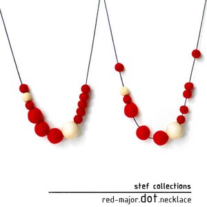 May include: Two necklaces with red and cream colored felt balls. The necklaces are on a white background. The text "stef collections red-major.dot.necklace" is below the necklaces.