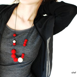 May include: A woman wearing a black cardigan over a gray t-shirt with a red and white felt bead necklace.
