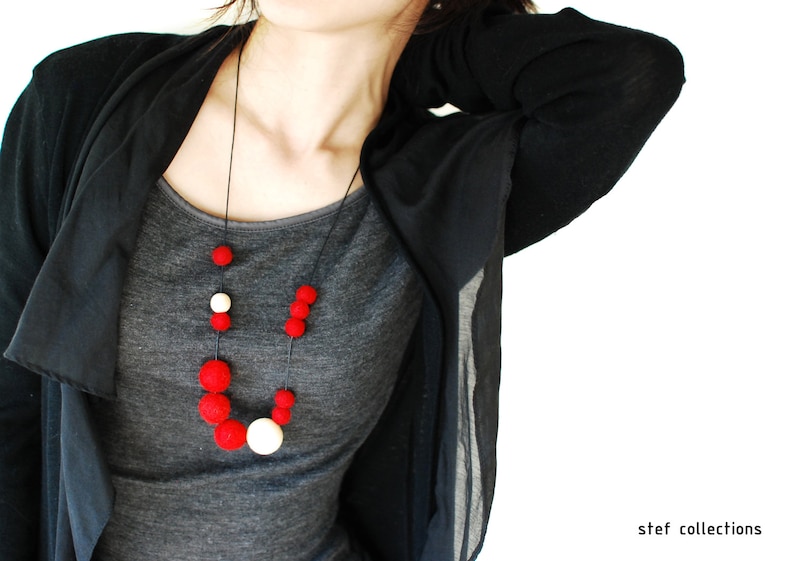 May include: A woman wearing a black cardigan over a gray t-shirt with a red and white felt bead necklace.