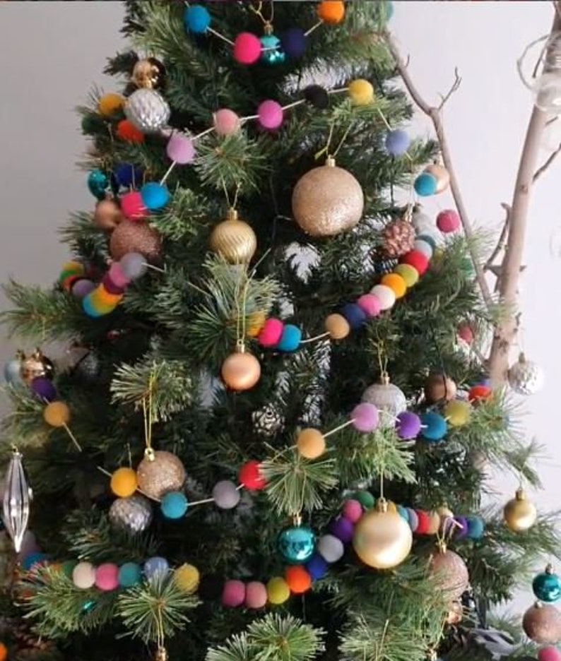 Puede incluir: Un &aacute;rbol de Navidad decorado con una guirnalda de bolas de fieltro de colores. La guirnalda presenta una variedad de colores, incluyendo rojo, azul, verde, amarillo y rosa. El &aacute;rbol tambi&eacute;n est&aacute; decorado con adornos dorados y plateados.
