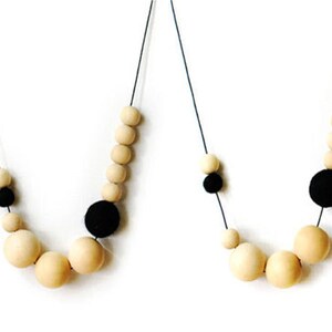May include: Two necklaces with wooden beads and black felt balls. The necklaces are made of a thin black cord.