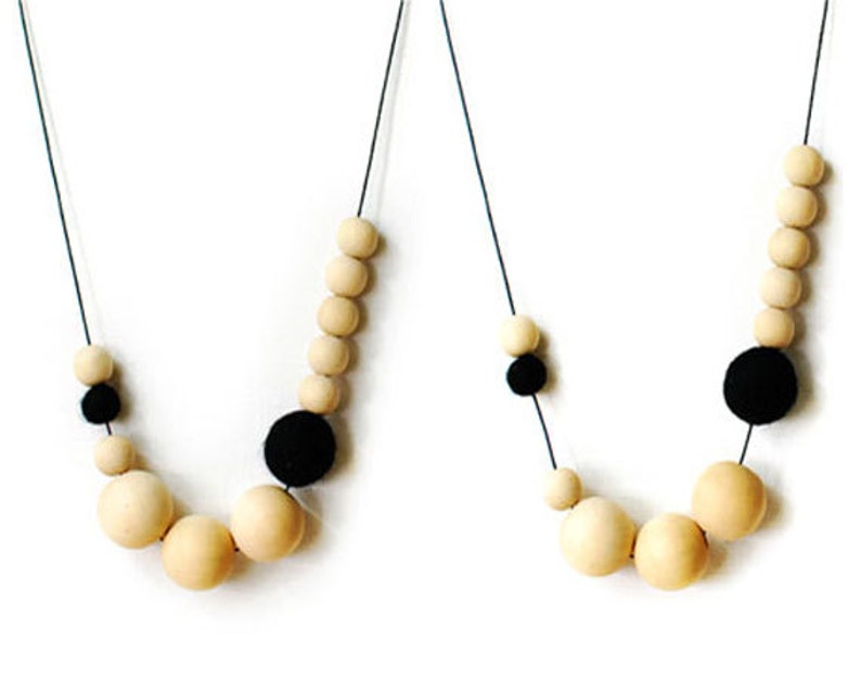May include: Two necklaces with wooden beads and black felt balls. The necklaces are made of a thin black cord.