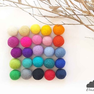 May include: A collection of 25 colorful felt balls arranged in a square pattern. The balls are in various shades of red, orange, yellow, green, blue, purple, and gray.