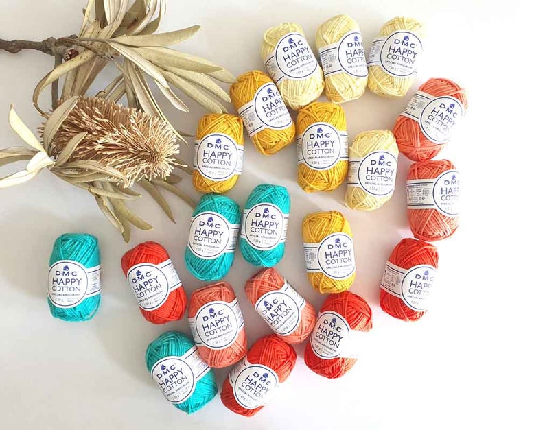 Pu&ograve; includere: Una collezione di gomitoli di lana colorati in tonalit&agrave; di arancione, giallo e turchese. Ogni gomitolo ha un'etichetta che recita "DMC Happy Cotton".