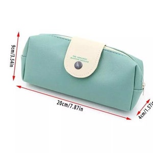 Pu&ograve; includere: Un astuccio per matite blu chiaro con una patta bianca e una chiusura a bottone. La patta ha il testo "The greatest happiness smiles" stampato. L'astuccio per matite misura 20 cm di lunghezza, 9 cm di altezza e 4 cm di larghezza.