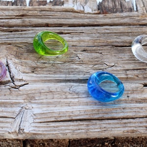 Op de afbeelding: Vier glazen ringen in verschillende kleuren: groen, paars, blauw en helder. De ringen zijn gerangschikt op een stuk verweerd hout.
