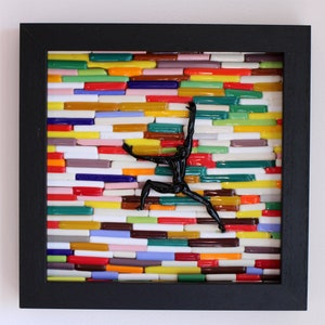 K&ouml;nnte beinhalten: Ein gerahmtes Mosaik-Kunstwerk mit einer schwarzen Silhouette einer Person, die eine Wand aus bunten Glasfliesen erklimmt.