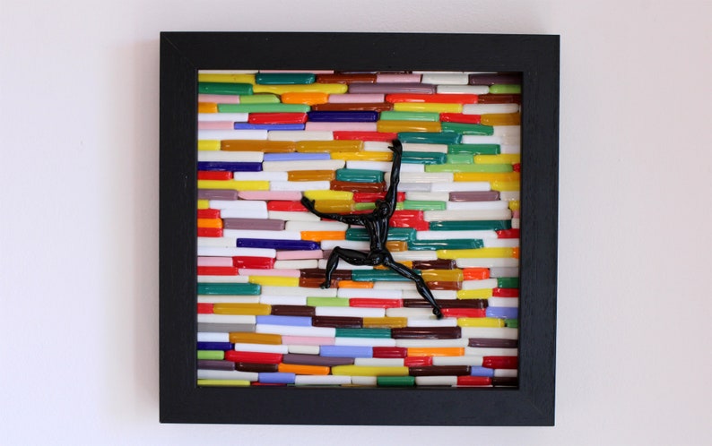 K&ouml;nnte beinhalten: Ein gerahmtes Mosaik-Kunstwerk mit einer schwarzen Silhouette einer Person, die eine Wand aus bunten Glasfliesen erklimmt.
