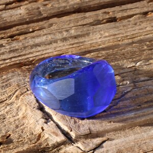 May include: A blue glass ring with a unique, irregular shape. The ring is made of clear glass with a blue tint and has a smooth, polished finish.