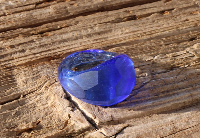 May include: A blue glass ring with a unique, irregular shape. The ring is made of clear glass with a blue tint and has a smooth, polished finish.