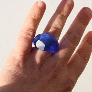 May include: A large, blue, faceted ring worn on a finger.